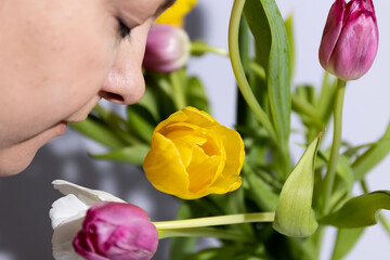 A woman smells colorful tulips in her hands in a room illuminated by sunlight. High quality photo
