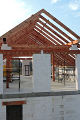 An "A" frame timber roof truss in a house under construction, walls made of aac blocks, a rough window opening, a reinforced brick lintel, a scaffolding, blue sky in the background