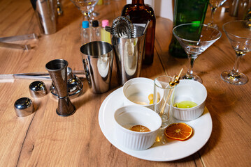 Cocktail Making Set with Citrus Garnishes on Wood. A cocktail preparation set with stainless steel shakers, jiggers, and a variety of citrus garnishes on a wooden bar table.
