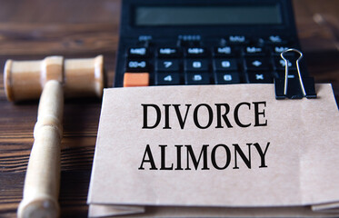 DIVORCE ALIMONY - words on light brown paper against the background of a calculator and a judge's gavel - obrazy, fototapety, plakaty
