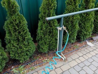 Lined communications for supplying air pressure with a compressor in the yard against the background of green trees that grow next to each other and cover the green metal fence behind them.