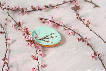 spring or easter background. delicate flowering branches with pink flowers and an egg-shaped gingerbread with an image of willow branches on a delicate pink-gray background.