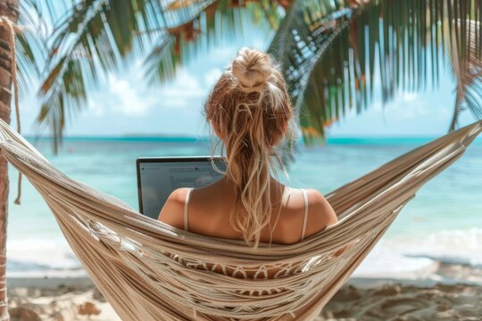 A woman is sitting on a hammock on a beach, using a laptop. Concept of relaxation and leisure, as the woman enjoys her time by the ocean while working on her laptop