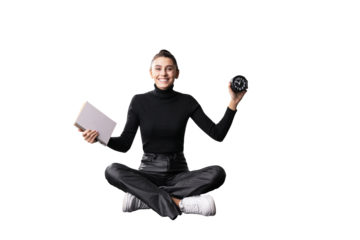 A smiling young woman sitting cross-legged, holding a notebook and clock, isolated on a white background, suggesting productivity and time management