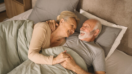 Embraced senior couple smiling and relaxing in bed