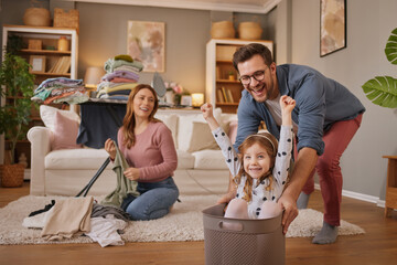 Little girl and dad laughing while playing with the laundry basket in living room
