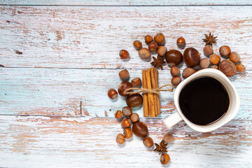 Topview of coffee in a white cup surrounded by chestnuts, hazelnuts, star anise and cinnamon on a...
