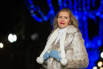 Portrait of a beautiful middle-aged woman in a fur coat in the lights of the evening city.