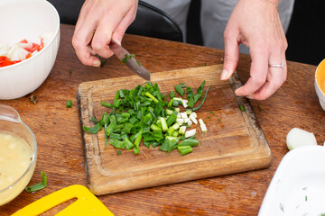 Hands chop green onions on a cutting board. Prepare vegetable salad.