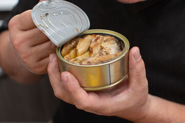 Hands open a metal fish can with sprats.