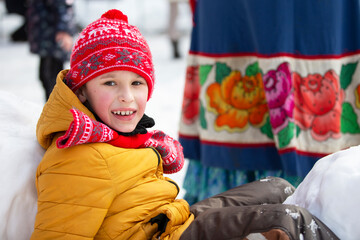 A child in winter clothes looks at the camera and smiles.