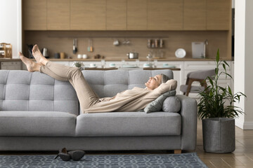 Peaceful happy mature woman lying on sofa relax in living room, enjoy lazy weekend at home,...