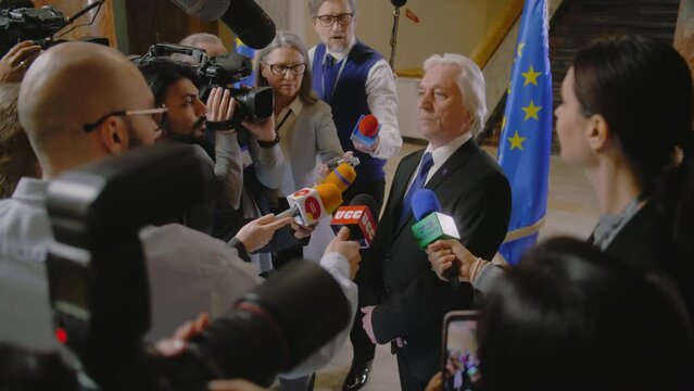 EU representative answers press questions and gives interview for TV breaking news. Senior consul surrounded by crowd of journalists. Political speech during press conference. State of the nation.