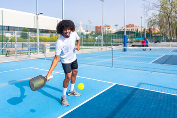 Smiling man with afro hair serving while playing pickleball