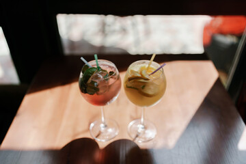 Two glasses of pink and yellow drinks sit on a table. The pink drink is a pink lemonade and the yellow drink is a lemonade with a slice of lime.