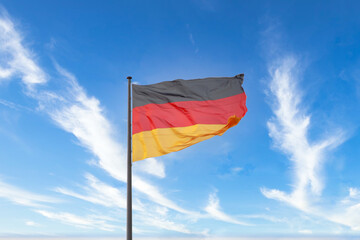 Germany flag waving in the wind on a flagpole, blue sky in the background. - 778032759