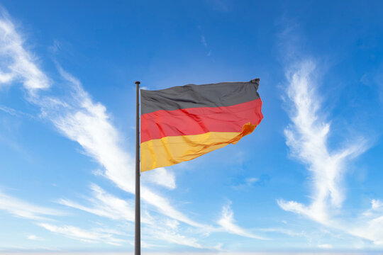Germany flag waving in the wind on a flagpole, blue sky in the background.