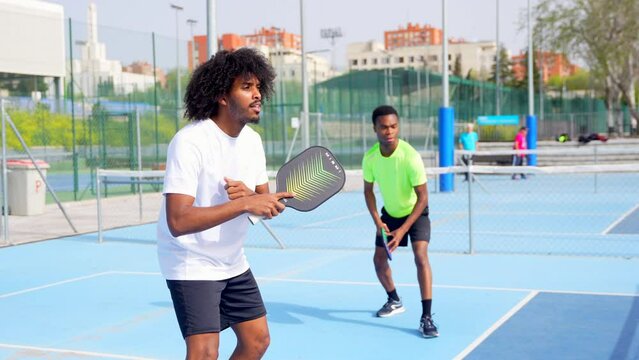 African young friends playing pickleball in an outdoor court in a sunny day