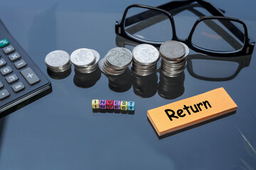 Business, invest, and return concept. Stacked coins, a calculator, an eyeglasses on the glass table. 
