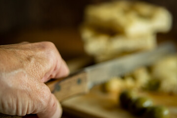 senior woman hand cutting Italian focaccia pizza bread with a knife 