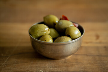 olive green pitted close up in a metal bowl with empty space on wooden board 