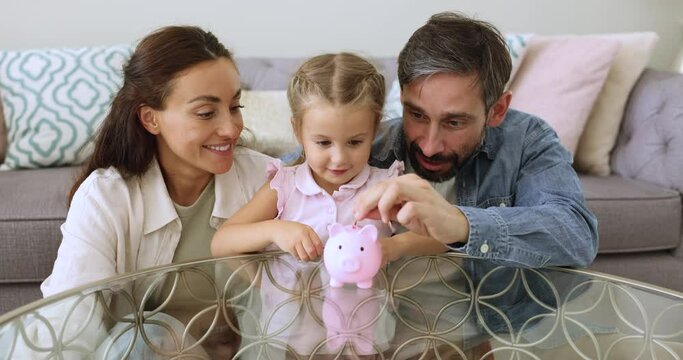 Little adorable daughter drop coins into piggy bank, loving parents teaching kid about being provident and saving money, good financial regular habit, save for future toy or long-term goals and dreams