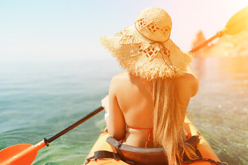 woman straw hat paddling a kayak on a lake. The sun is shining brightly, creating a warm and...