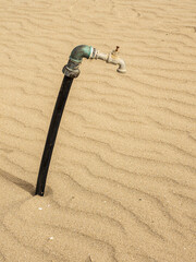 Tubo dell'acqua sulla sabbia. Rubinetto abbandonato: simbolo della crisi idrica e del degrado ambientale