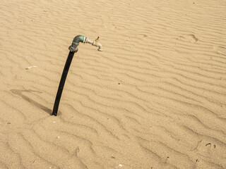 Tubo dell'acqua sulla sabbia. Rubinetto abbandonato: simbolo della crisi idrica e del degrado ambientale
