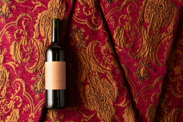 Bottle of red wine on a retro tapestry with dark red and golden floral ornament.