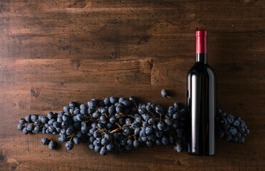 Blue grapes and bottle of red wine on an old wooden table.