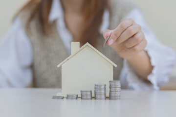women hand put money coins into house-shaped piggy bank on the table for saving money for buying a...