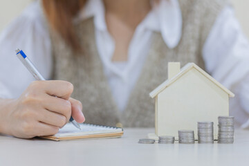 Female hands taking notes Financial statistics. house-shaped piggy bank  for saving money for...