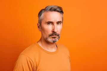 A man with a beard and gray hair is wearing an orange shirt