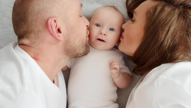 Newborn baby with happy parents, top view. Happy family.  Healthy newborn baby in a white t-shirt with mom and dad. Close up Faces of the mother, father and infant baby.  Cute  Infant boy and parents