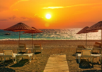 beautiful pebble beach and emerald water.orange colorful bright sunrise on the beach.  sun lounger...