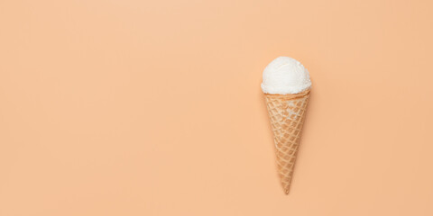 Ice cream in a waffle cone on a pastel peach background. Top view, flat lay, banner.