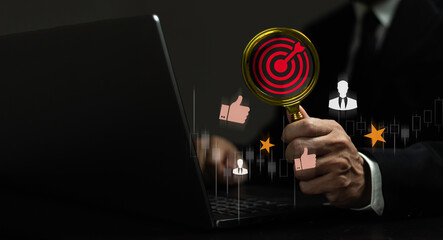 A man is holding a magnifying glass over a laptop screen with a red target on it