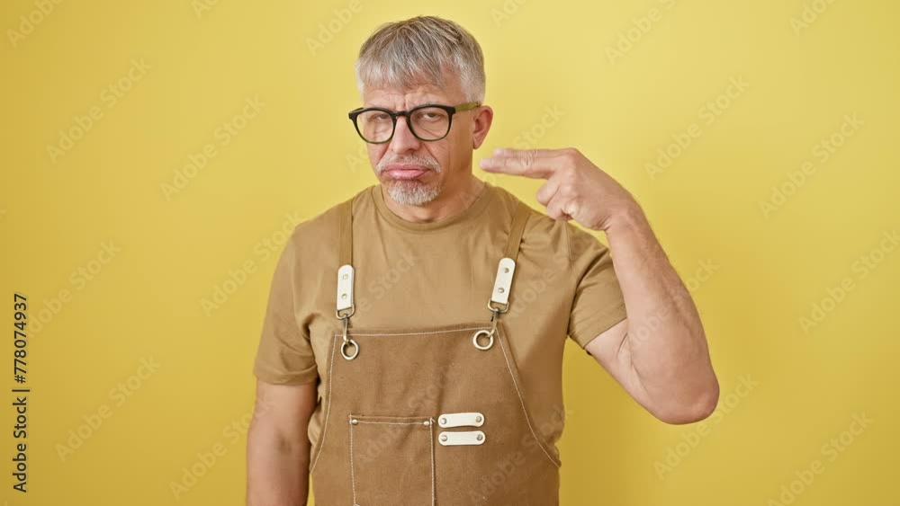 Poster depressed middle age man, grey-haired and bespectacled, standing isolated on yellow background. maki