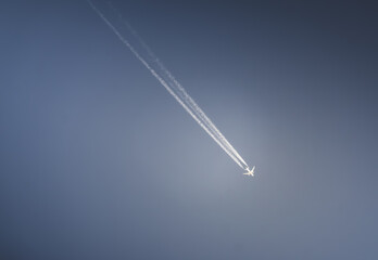 An airplane flies in a blue cloudy sky leaving a contrail, abstraction for background