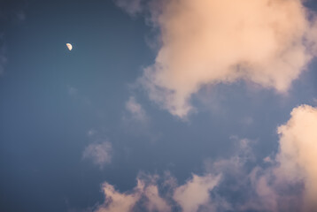 The moon glows in the evening blue cloudy sky, minimalistic evening sky for background
