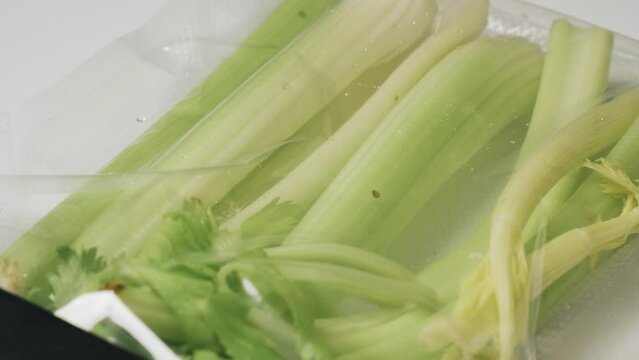 A man uses a vacuum sealer to vacuum seal celery into a bag. Close-up.