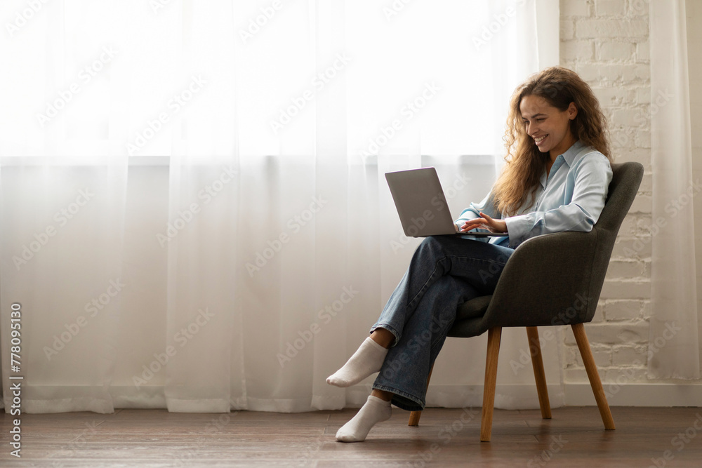 Wall mural cheerful happy lady enjoy online work, using laptop, sitting in chair at home, free space. modern pr