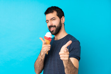 Young man with a cornet ice cream over isolated blue background pointing to the front and smiling