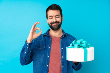 Young handsome man with a big cake over isolated blue background in zen pose