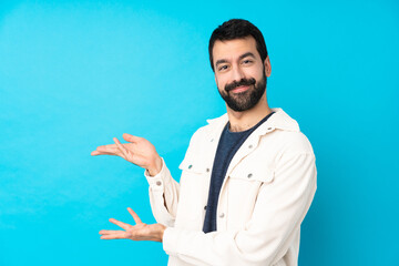 Young handsome man with white corduroy jacket over isolated blue background extending hands to the...