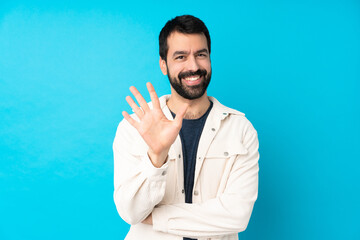 Young handsome man with white corduroy jacket over isolated blue background counting five with...