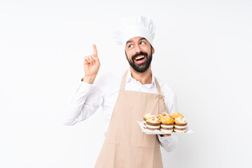 Young man holding muffin cake over isolated white background intending to realizes the solution while lifting a finger up