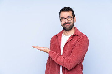 Young caucasian man wearing corduroy jacket over blue background presenting an idea while looking...