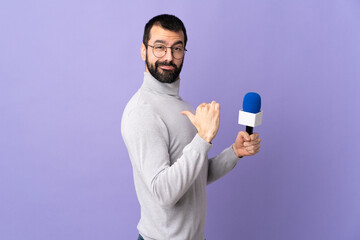 Adult reporter man with beard holding a microphone over isolated purple background proud and...